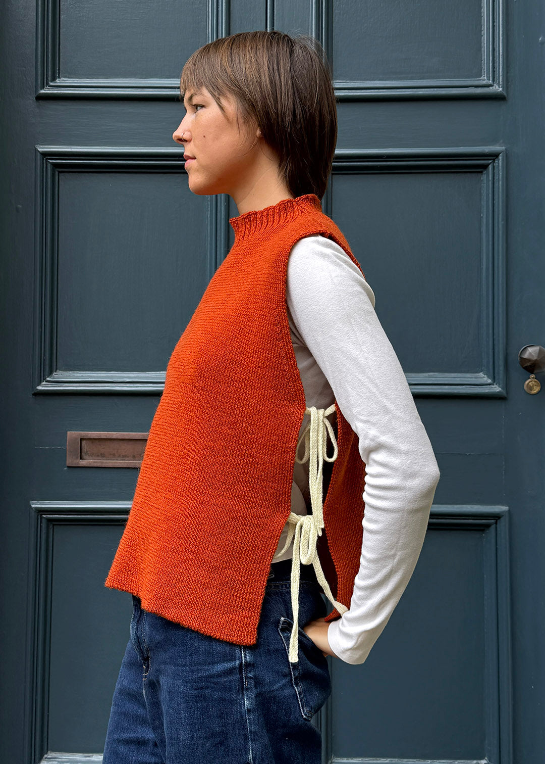 Orange knitted Flora Studio vest with butter yellow ties shown on model.