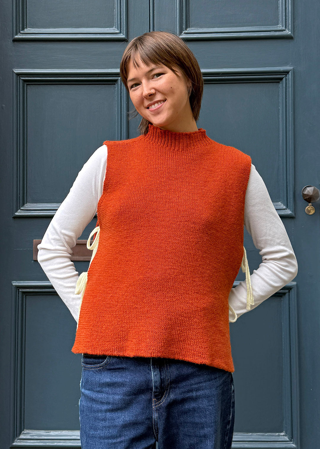 Orange knitted Flora Studio vest with butter yellow ties shown on model.