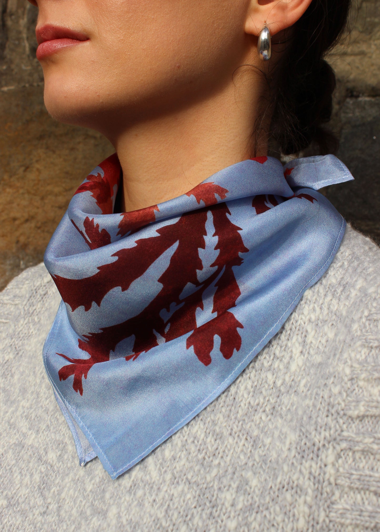 The Drift silk scarf features a collaged print of seaweeds in vibrant reds on a light blue background.