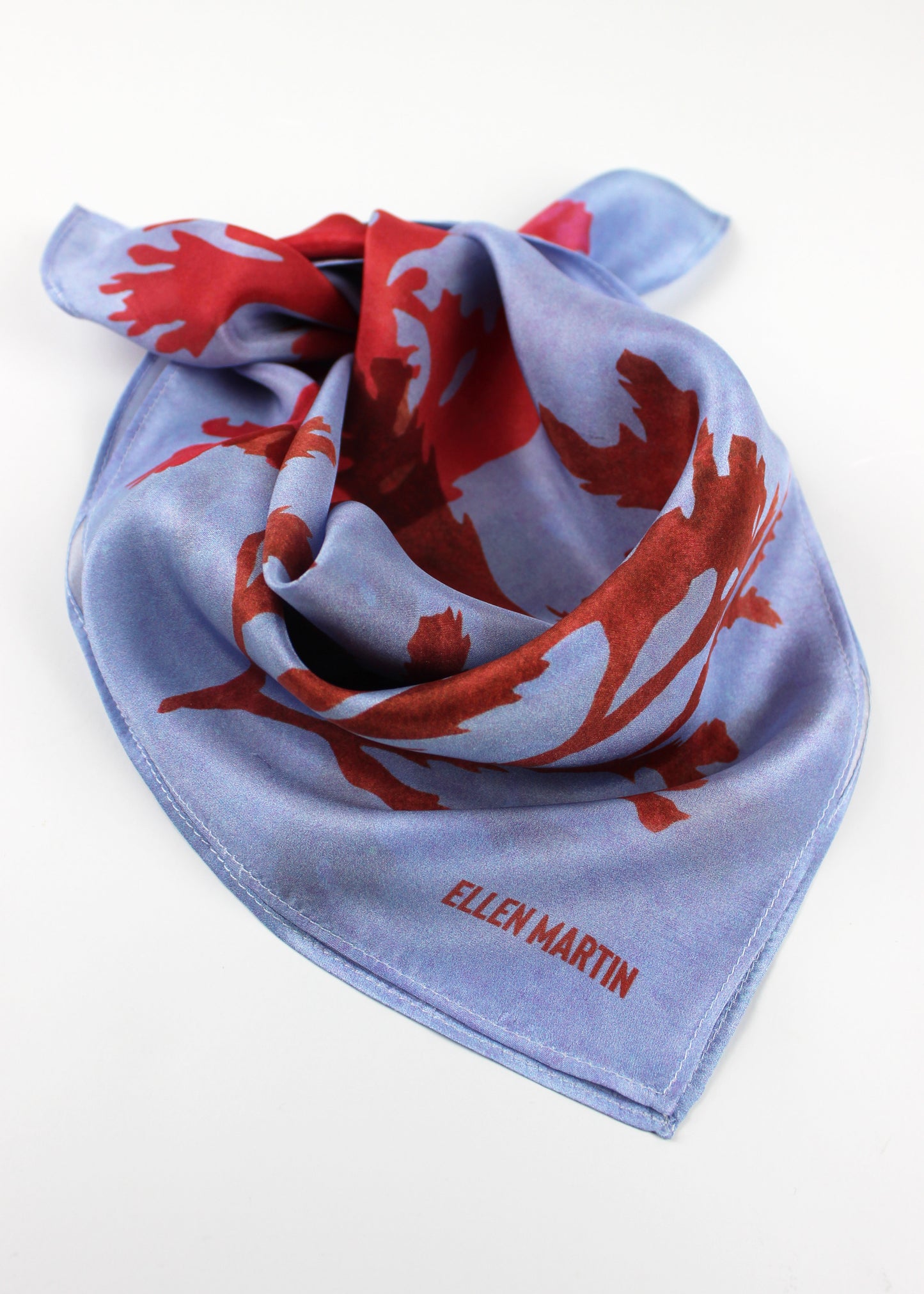 The Drift silk scarf features a collaged print of seaweeds in vibrant reds on a light blue background.