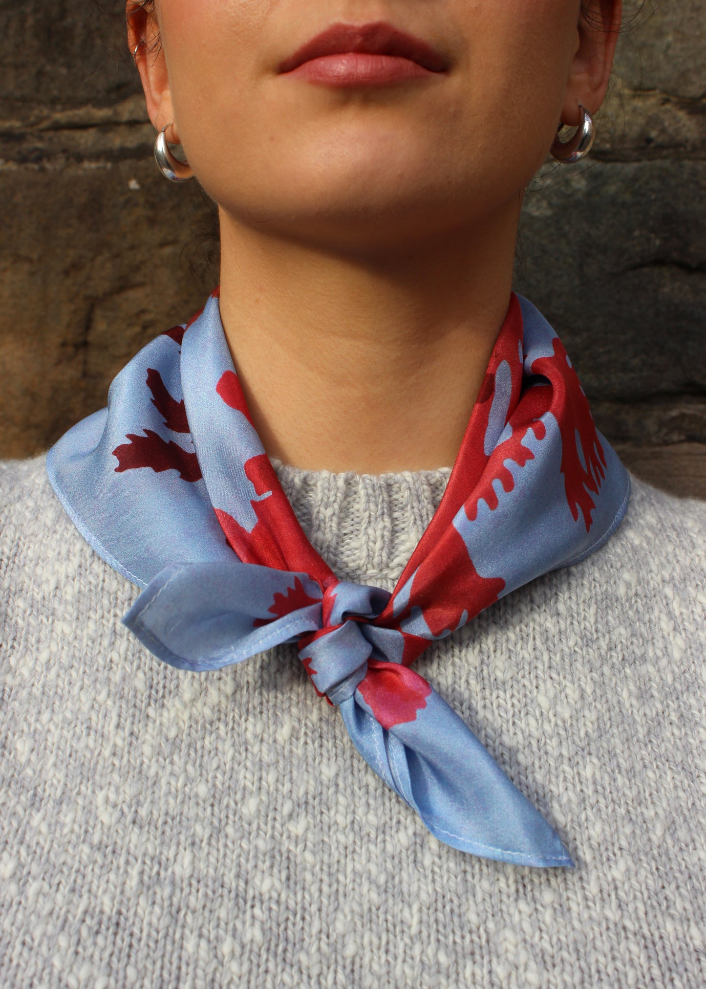 The Drift silk scarf features a collaged print of seaweeds in vibrant reds on a light blue background.