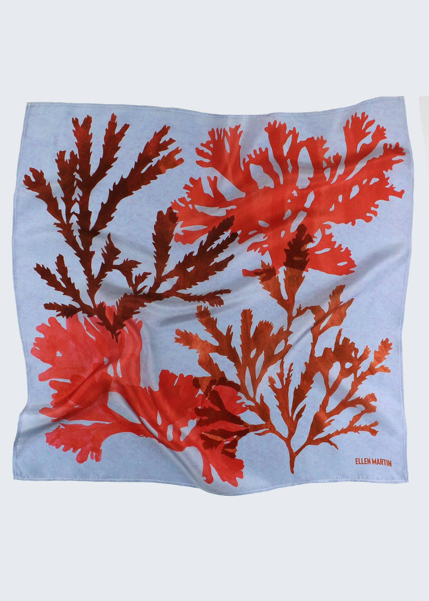 The Drift silk scarf features a collaged print of seaweeds in vibrant reds on a light blue background.