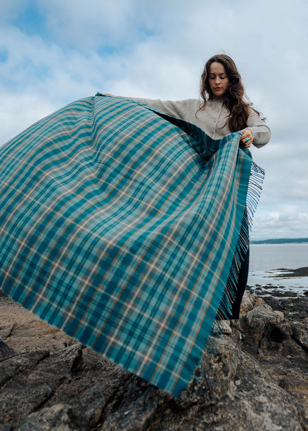 Model holding a lambswool teal tartan blanket on a beach.