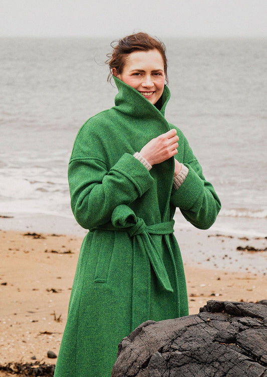 Harris Tweed cora coat in emerald green shown worn at the beach. Scottish Textiles Showcase.