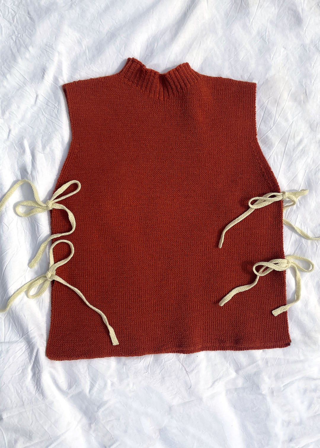 Orange knitted Flora Studio vest with butter yellow ties on a white background.