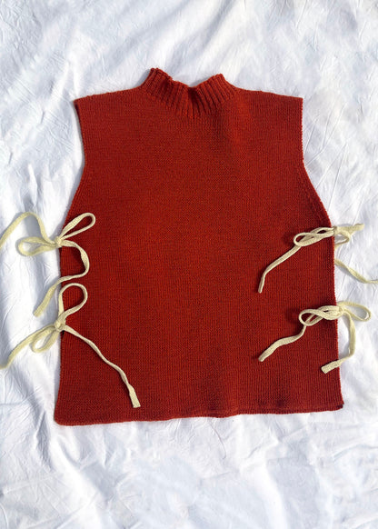 Orange knitted Flora Studio vest with butter yellow ties on a white background.