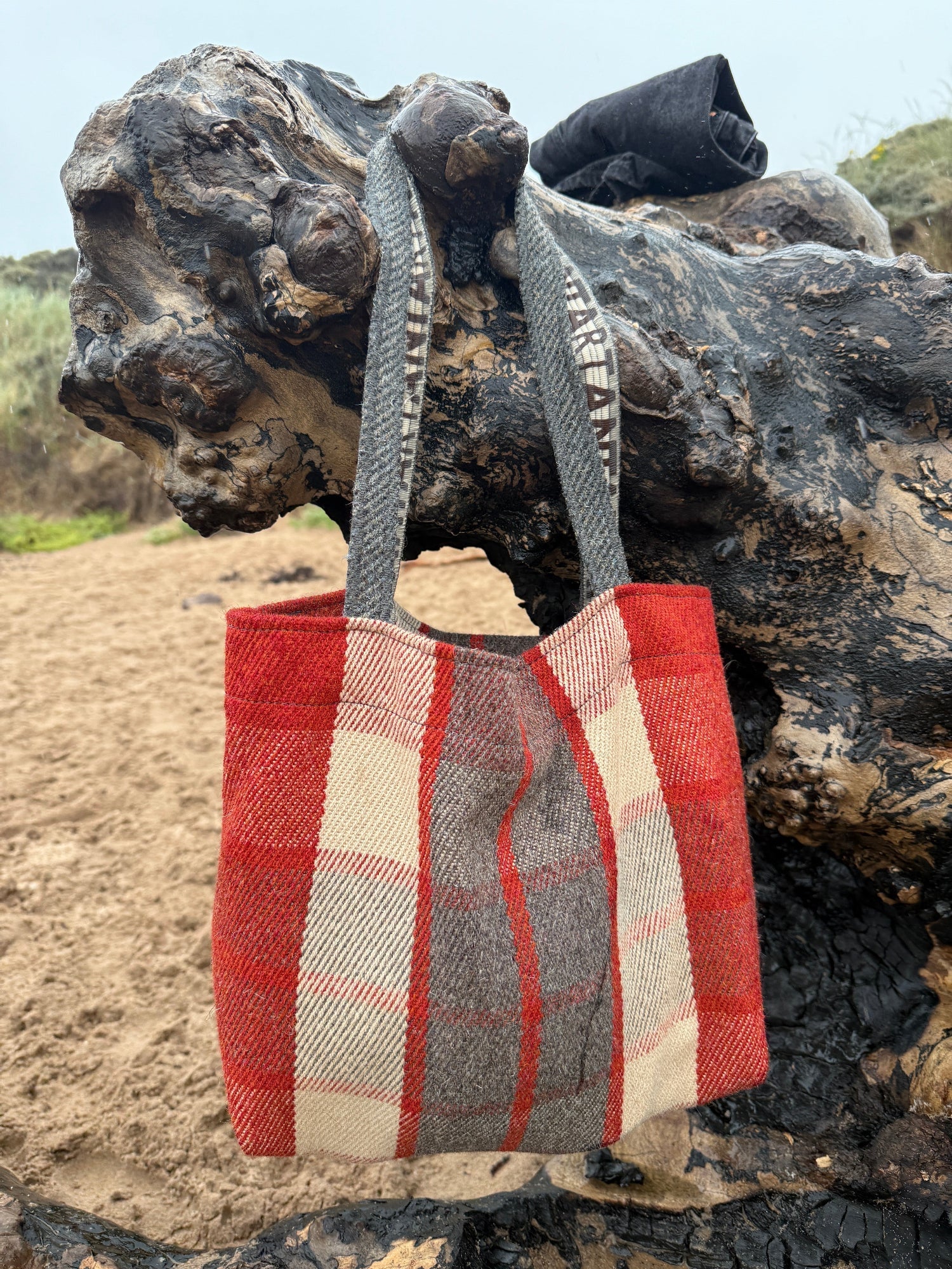 Red and beige checkered bag attached to a piece of drift wood on the beach