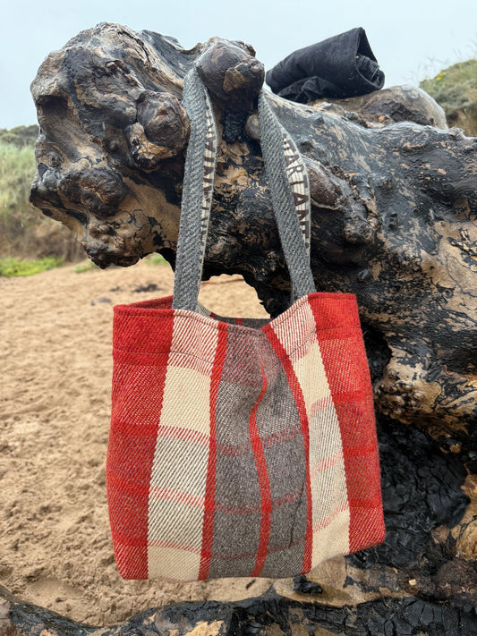 Red and beige checkered bag attached to a piece of drift wood on the beach