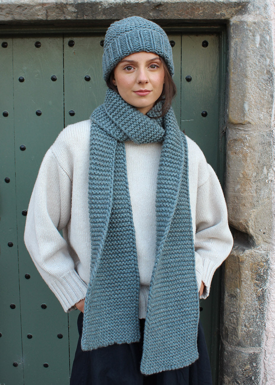 British wool chunky steel blue knitted scarf modelled with matching hat. Scottish Textiles Showcase.