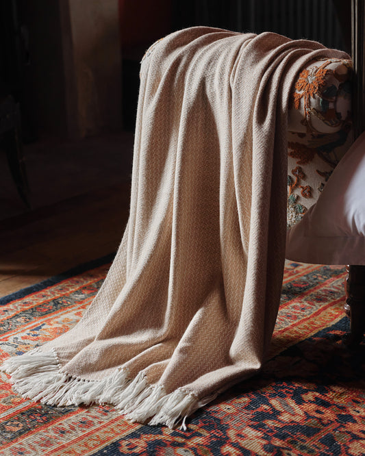 Araminta Campbell kingsize undyed alpaca throw in Woodland Inkcap pattern. Shown draped in rustic interior with patterned rug