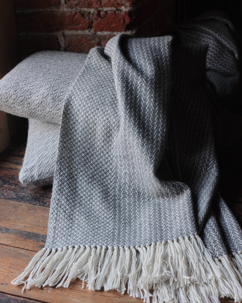 Araminta Campbell kingsize undyed alpaca throw in Woodland Inkcap pattern. Shown with cushions in rustic wooden interior.