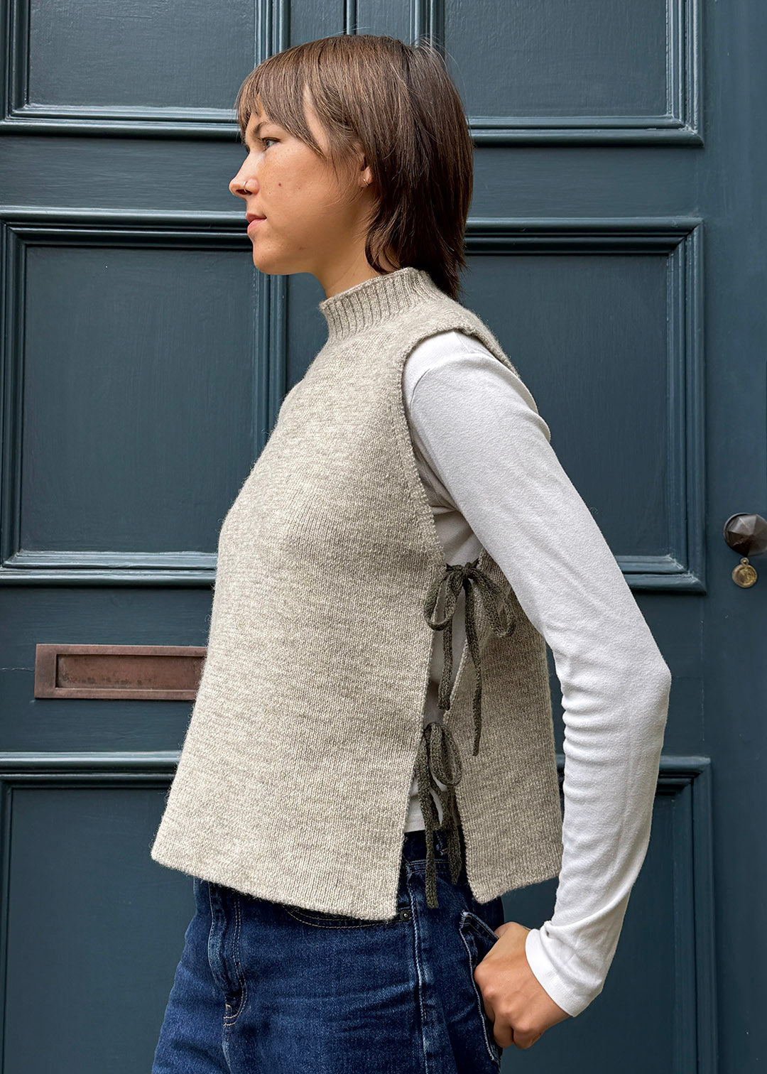 Oat knitted Flora Studio vest with olive green ties shown on model. 