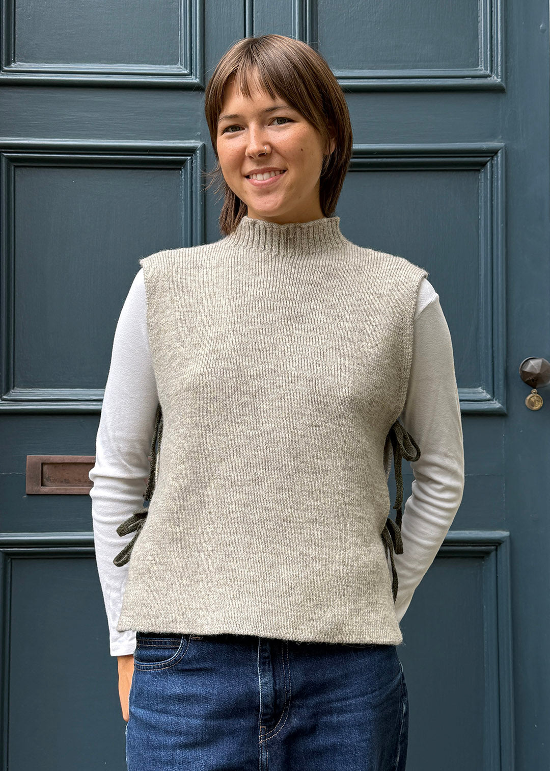 Oat knitted Flora Studio vest with olive green ties shown on model. 