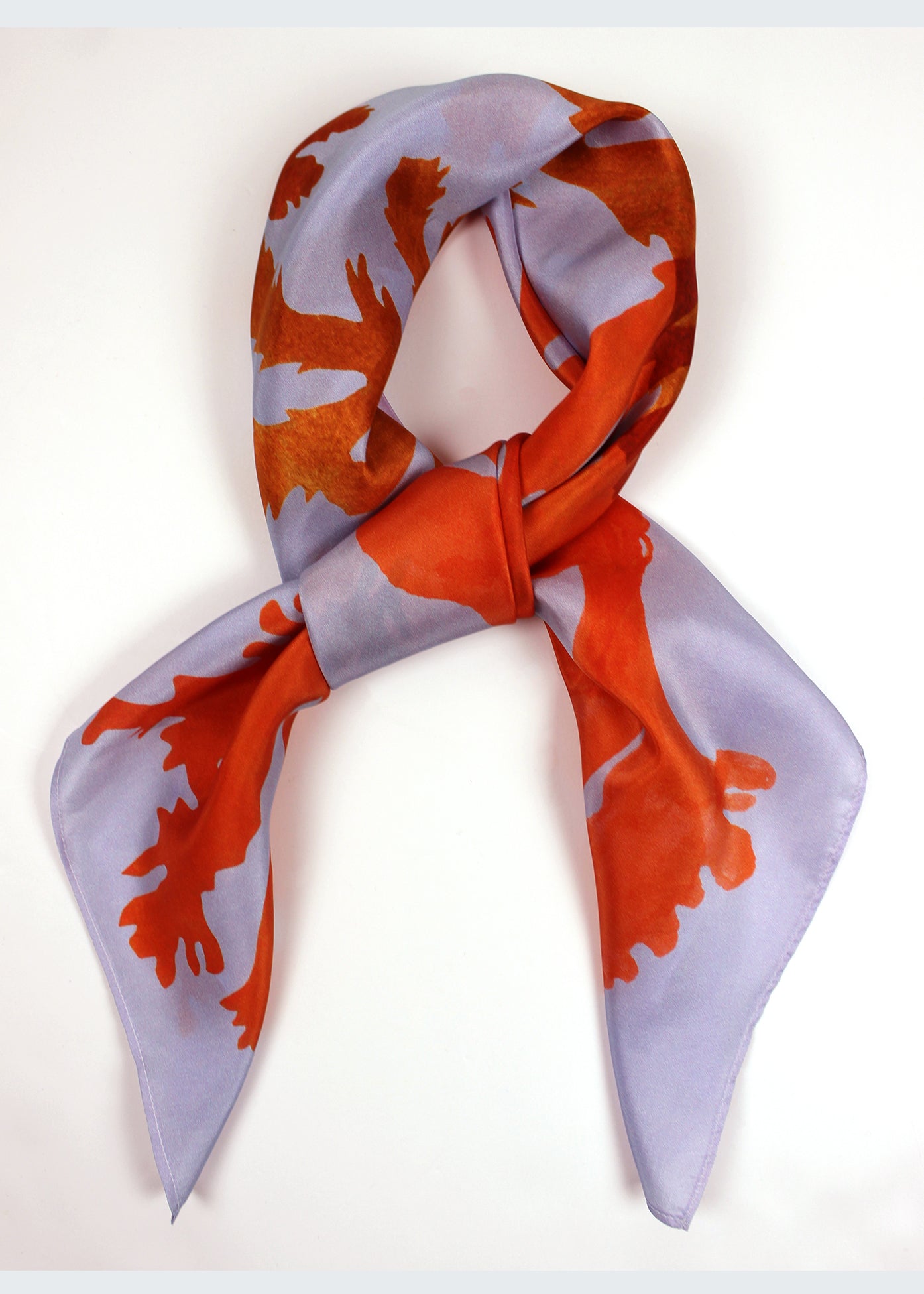 The Drift silk scarf features a collaged print of seaweeds in vibrant oranges on a lilac background.