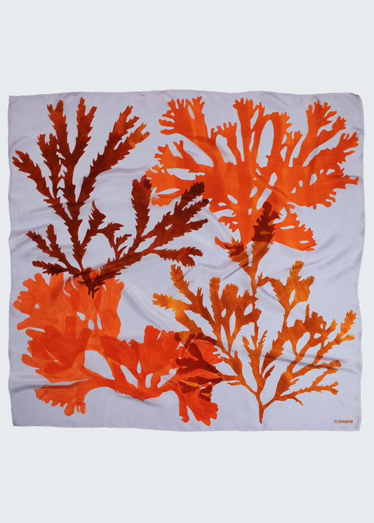 The Drift silk scarf features a collaged print of seaweeds in vibrant oranges on a lilac background.