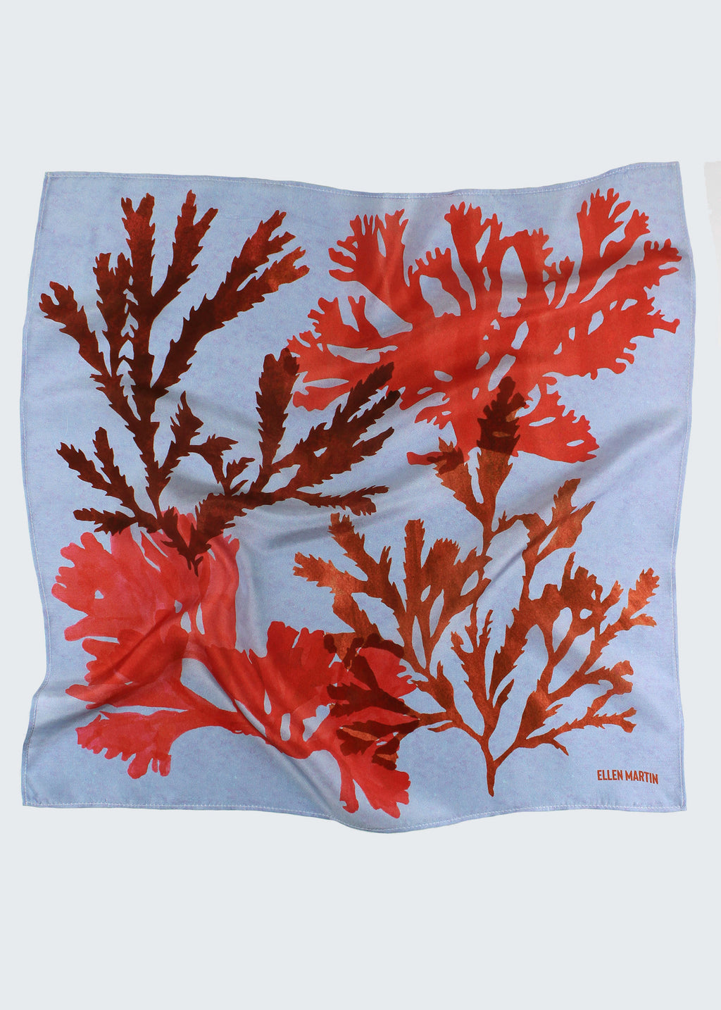 The Drift silk scarf features a collaged print of seaweeds in vibrant reds on a light blue background.