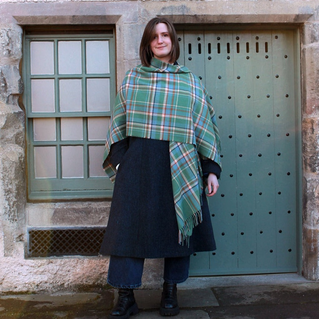 Araminta Campebell Highlands at Dawn woven lambswool serape with tassels. Woven with a hazy shades of green and blue with a touch of burnt orange and peach white . Scottish Textiles Showcase.