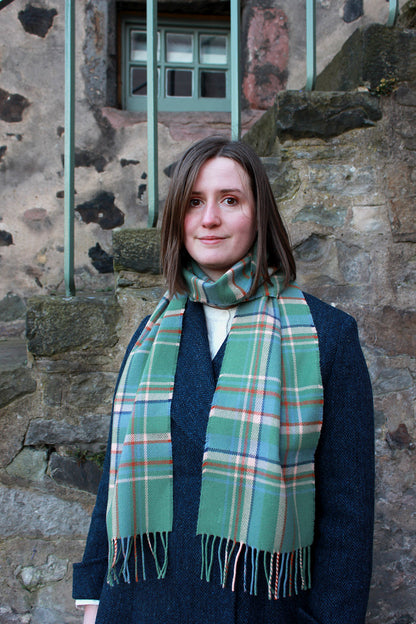 Araminta Campebell Highlands at Dawn woven lambswool scarf with tassels. Woven with a hazy shades of green and blue with a touch of burnt orange and peach white . Scottish Textiles Showcase.