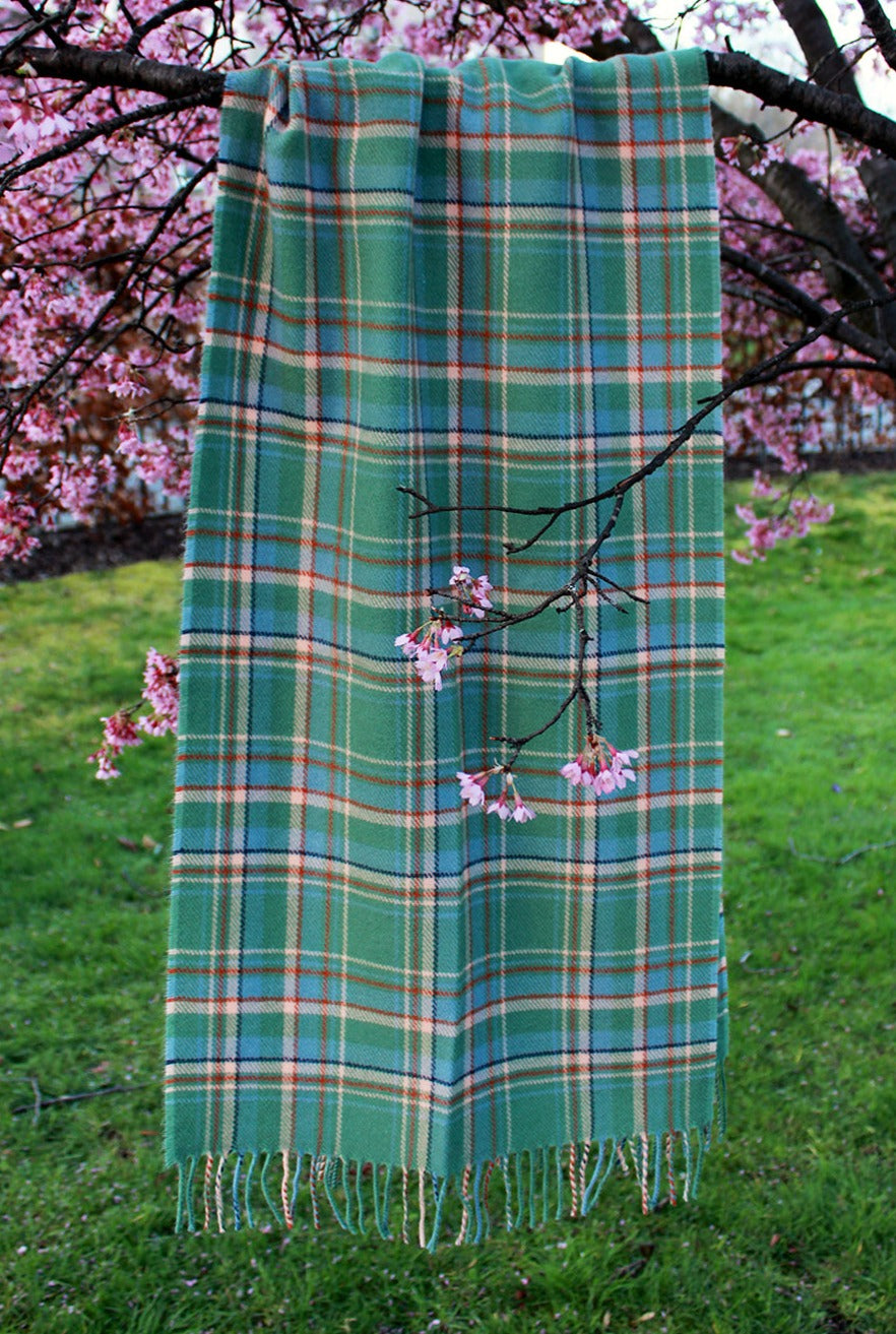 Araminta Campebell Highlands at Dawn woven lambswool shawl with tassels. Woven with a hazy shades of green and blue with a touch of burnt orange and peach white . Scottish Textiles Showcase.