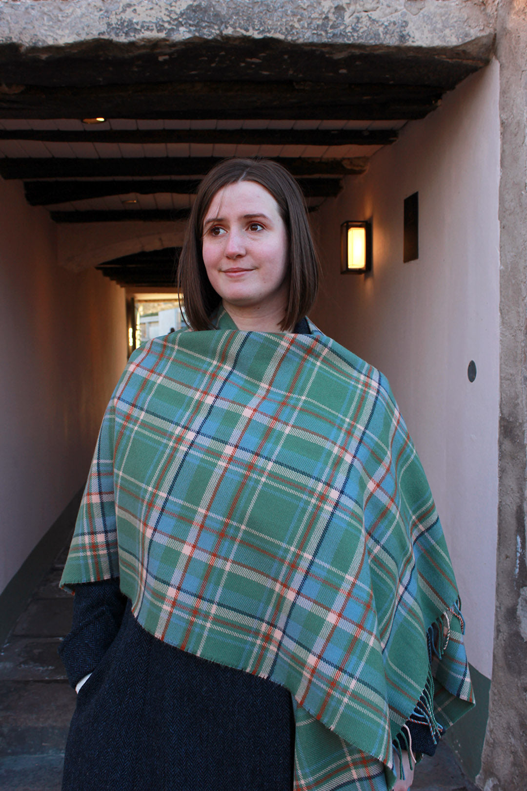 Araminta Campebell Highlands at Dawn woven lambswool serape with tassels. Woven with a hazy shades of green and blue with a touch of burnt orange and peach white . Scottish Textiles Showcase.