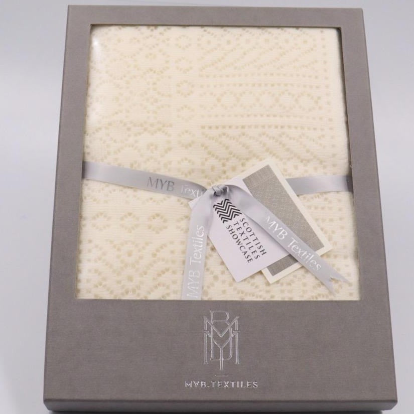 An ivory cotton lace baby shawl, folded, wrapped in a silver ribbon, and in a grey gift box. 