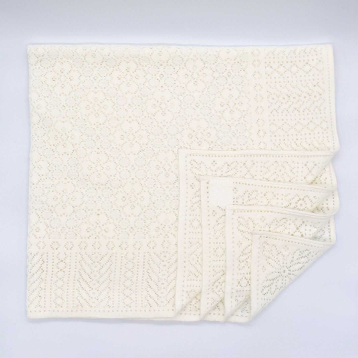An ivory cotton lace baby shawl with four layers in the bottom right corner decoratively folded towards the centre. 