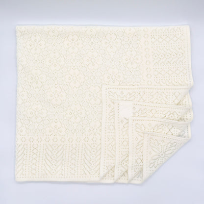 An ivory cotton lace baby shawl with four layers in the bottom right corner decoratively folded towards the centre. 