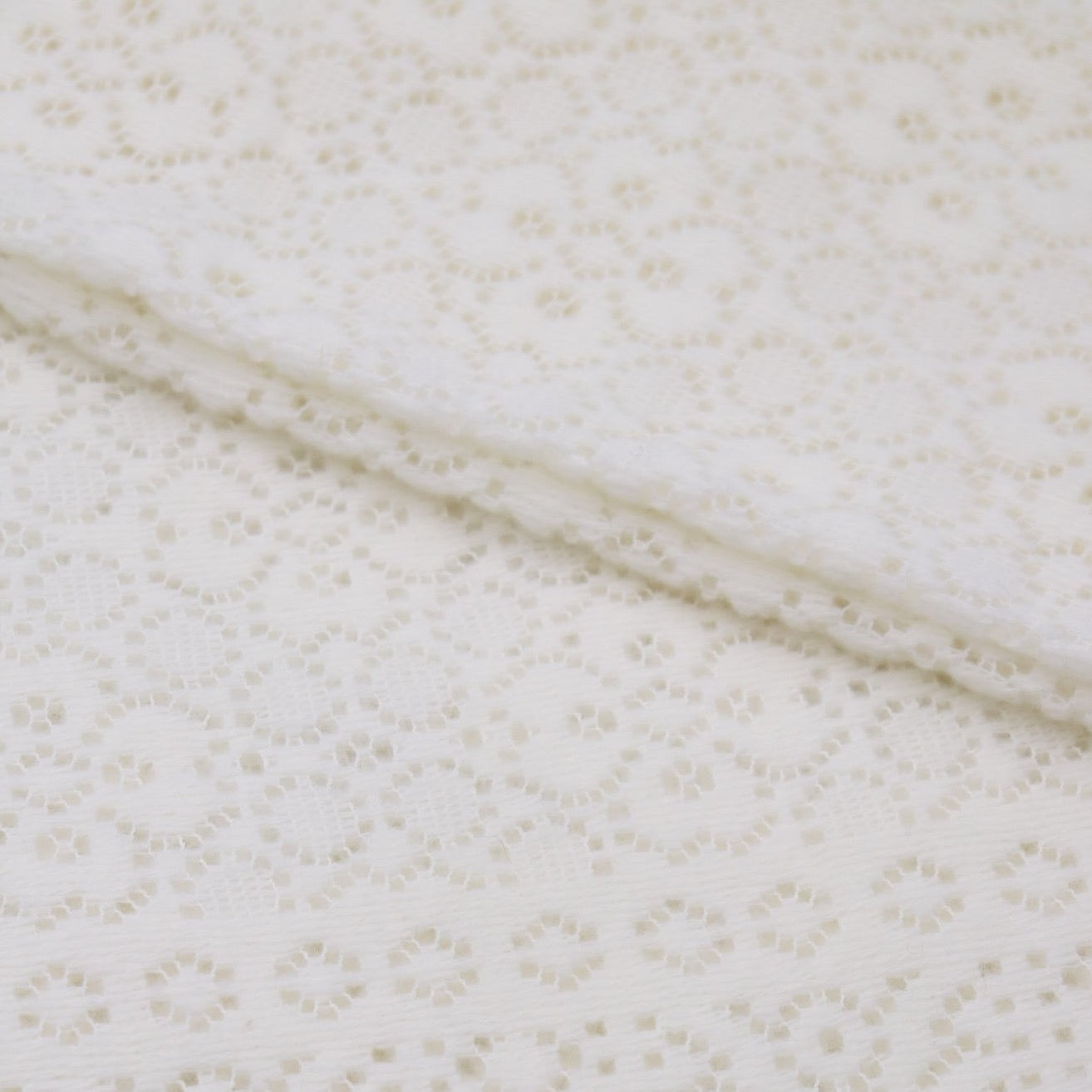 A close up folded detail of an ivory cotton lace baby shawl. 