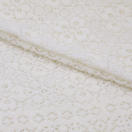 A close up folded detail of an ivory cotton lace baby shawl. 