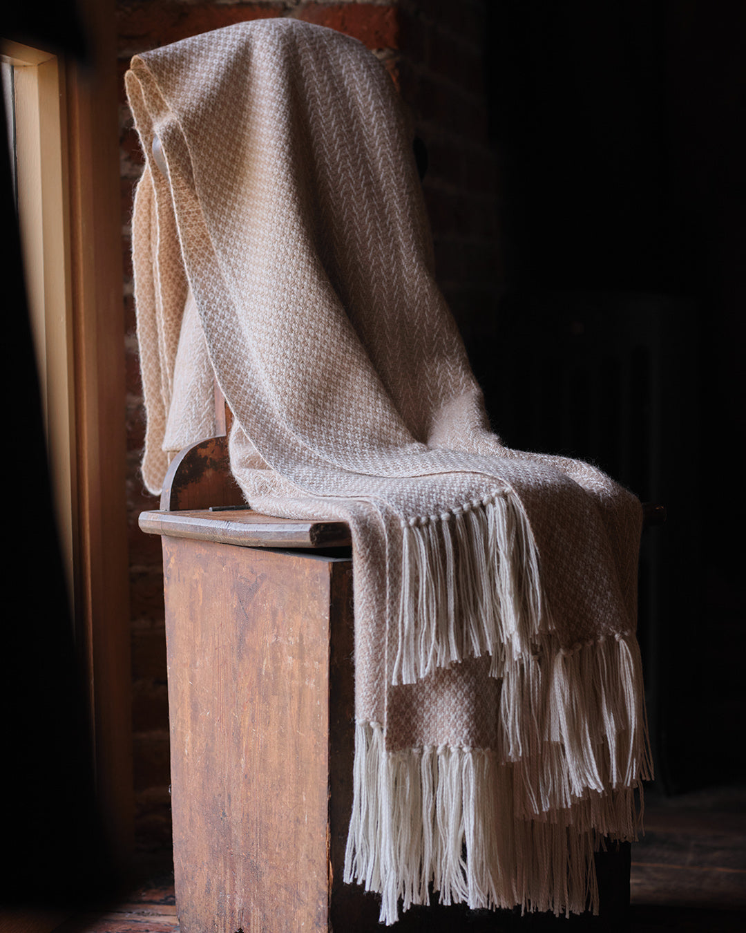 Araminta Campbell kingsize undyed alpaca throw in Woodland Inkcap pattern. Shown draped in rustic interior.