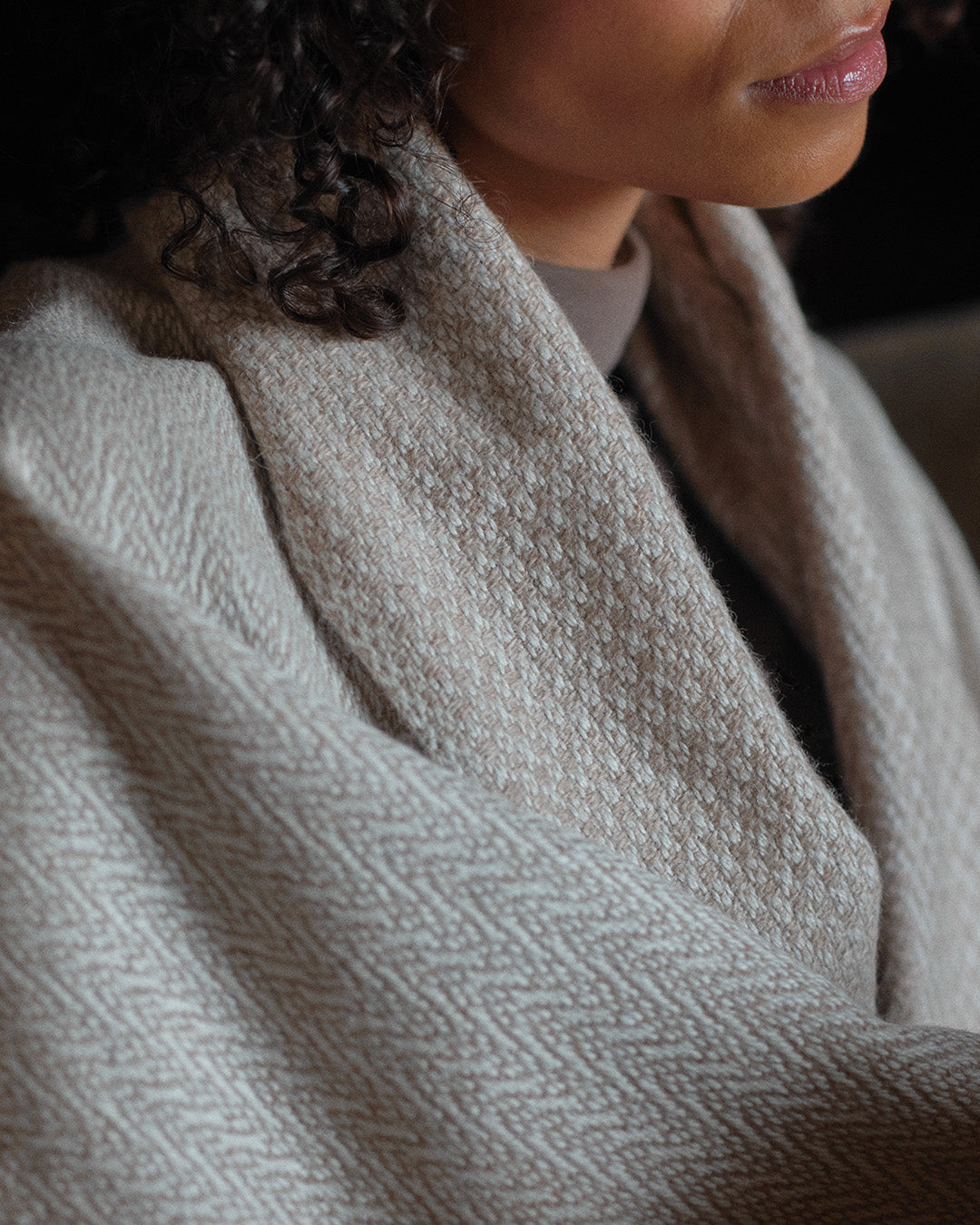 Araminta Campbell kingsize undyed alpaca throw in Woodland Inkcap pattern. Shown wrapped around woman on sofa.