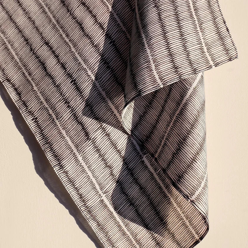 Black and white tatami print silk scarf, hanging on plain background.