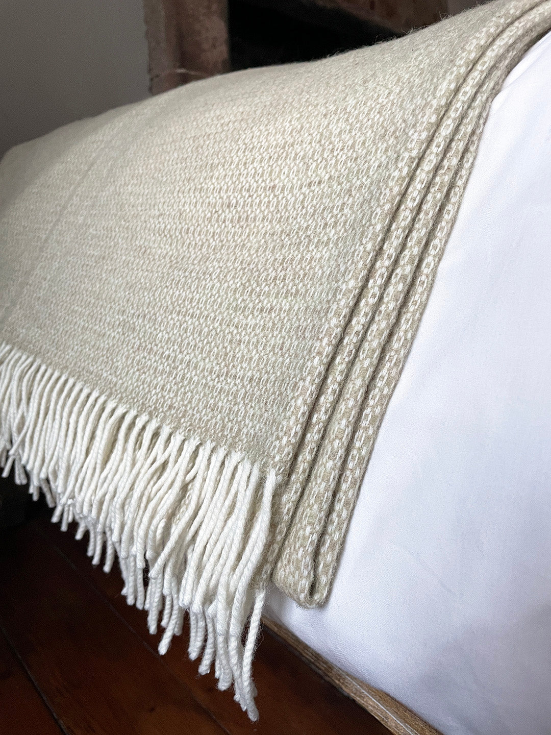Generously sized pure merino lambswool throw woven in a delicate pattern in pale moss green and cream, shown draped over end of a bed.