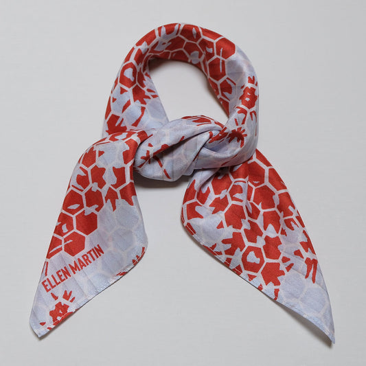 Small square silk scarf in a red, pale blue and cream geometric repeat pattern, shown tied in bow against plain background.