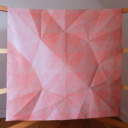 Large square silk scarf in a subtle pattern in shades of coral, peach and tan, shown hanging on wooden frame.
