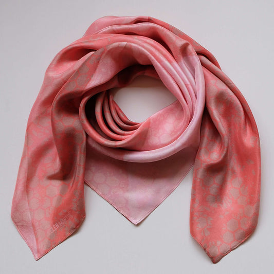 Large square silk scarf in a subtle pattern in shades of coral, peach and tan, shown draped against plain background.