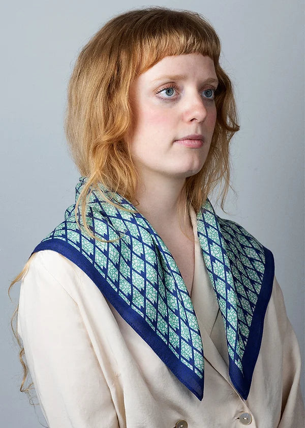 Wool and silk blend square scarf with intricate repeat pattern in blue and teal on an ivory background, shown on model.